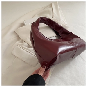 Close-up of a burgundy patent leather handbag on a beige blazer with a vintage aesthetic