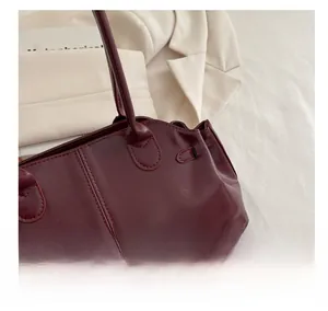 Close-up of glossy wine red leather surface and neat stitching on a minimalist handbag