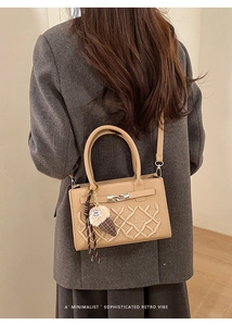 Détail d'un sac à bandoulière carré beige avec broderie GA et pendentif peluche