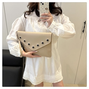 Chic beige rivet handbag with V-shaped flap and wristlet strap shown in a lifestyle mirror shot