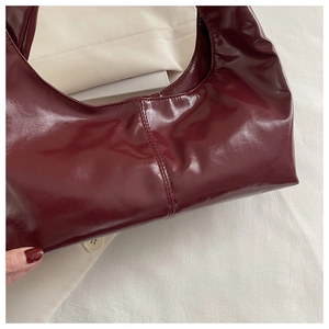 Detail of wine red glossy patent leather tote with seamless curved handle and vertical stitching