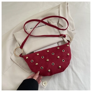 Détail du sac demi-lune bordeaux avec texture daim et rivets dorés sur une veste chic