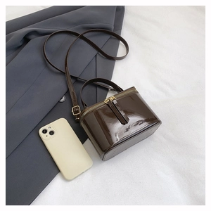 Detail view of mini brown patent leather box bag with dual gold zippers and sleek top handle