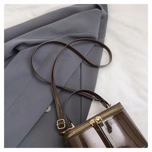 Detail of dark brown patent leather mini barrel bag with gold-tone hardware on grey blazer