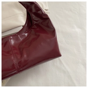 Detail of wine red glossy handbag featuring precise stitching and shiny patent texture
