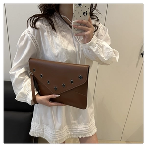 Detail view of a brown leather envelope clutch bag featuring metal rivet eyelet accents