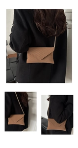 Brown envelope chain bag with gold strap shown on a black coat for styling view