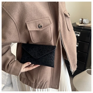 Sac enveloppe imprimé léopard avec chaîne dorée porté par un mannequin en intérieur