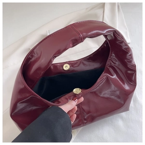 Detail of burgundy glossy tote bag showing magnetic buckle and black fabric lining