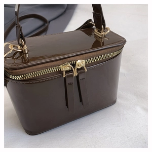 Close-up of shiny dark chocolate patent leather box bag with golden zippers and metal hardware