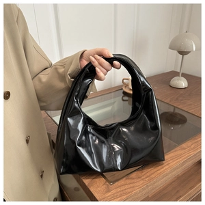 Close-up of black glossy patent leather shoulder bag in a stylish office setting