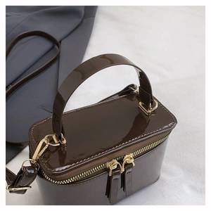 Detail view of glossy chocolate brown patent leather bag with gold metal zippers