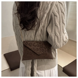Détail du sac enveloppe à imprimé léopard avec chaîne dorée sur un pull en maille beige
