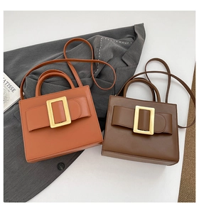 Detail view of two chic square leather handbags with gold buckles on a grey blazer suit