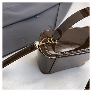 Detail of glossy brown patent leather handbag with gold metal zipper and stitching