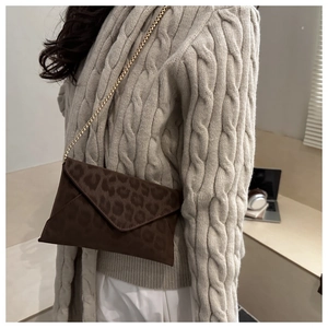 Détail du sac enveloppe léopard avec chaîne dorée sur un pull en maille