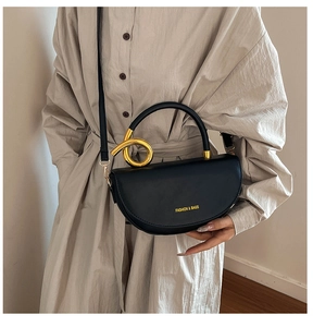 Detail of black leather saddle bag with gold metal handle on a beige dress model