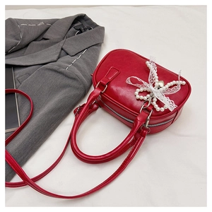 Détail du sac rouge chic avec nœud en perles, dentelle et pendentif cœur sur le lit