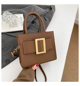 Detailed close-up of brown textured leather bag with vintage gold square metal buckle