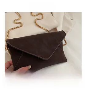 Detail of dark brown envelope bag with lychee grain texture and golden chain strap
