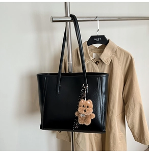 Detail of black faux leather tote bag with a cute plush dog pendant and long shoulder straps