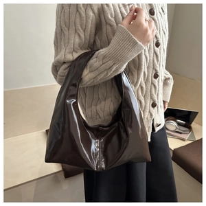 Detail of dark brown glossy patent leather hobo bag worn by model in a warm setting