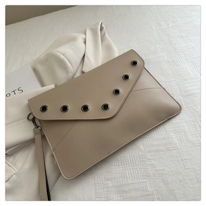 Detail view of beige envelope clutch bag featuring silver eyelet studs and wristlet strap