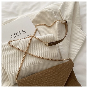 Detail of brown woven textured crossbody bag with gold chain strap on soft corduroy