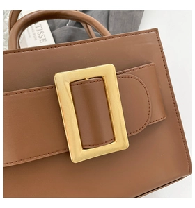 Close-up of a brown matte leather bag featuring a large gold square buckle and fine stitching