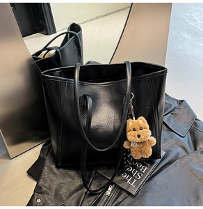 Detailed texture of black leather tote bag with a cute brown teddy dog pendant charm