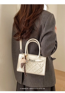 Detail of white square handbag with floral embroidery and ice cream charm on model