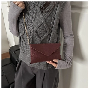 Détail du sac enveloppe bordeaux avec chaîne dorée porté sur un pull gris