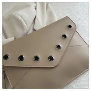 Detailed view of beige envelope clutch with asymmetric V-cut and metal eyelet studs