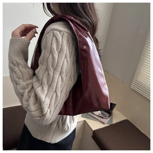 Side view of a burgundy patent leather hobo bag worn by a model in a cozy sweater