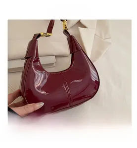 Detail of burgundy patent leather handbag featuring a knotted handle and gold hardware