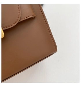 Detailed macro view of the brown leather bag texture with fine stitching and gold buckle
