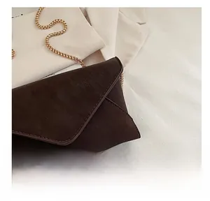 Detail of dark brown faux suede envelope bag featuring a gold snake chain strap