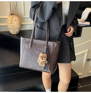 Deep brown tote bag detail with plush bear charm and striped tassel accessory