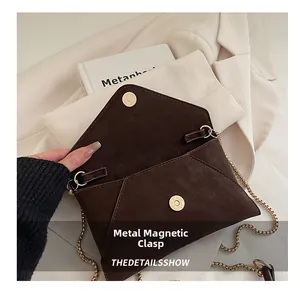 Detailed close-up of the magnetic clasp and gold chain on the dark brown envelope bag
