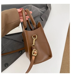 Detail of dark brown leather tote bag with gold metal buckle and adjustable strap