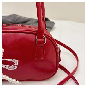 Détail d'un sac à main rouge brillant orné d'un nœud en dentelle blanche et de perles