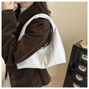 Close-up of a white glossy hobo shoulder bag worn by a model in a minimalist setting
