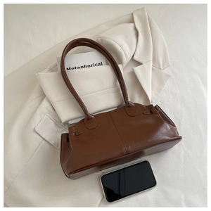 Close-up of caramel pleated faux leather handbag styled on white suit with lifestyle props