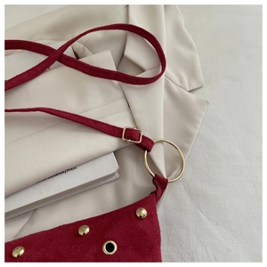 Gros plan détaillé du sac à bandoulière en daim rouge foncé avec rivets et anneaux dorés