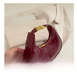 Close-up of red patent leather dumpling bag with gold buckle on beige blazer