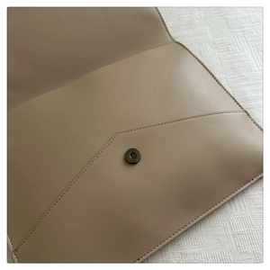 Detail view of the metal magnetic clasp on a minimalist taupe faux leather envelope bag