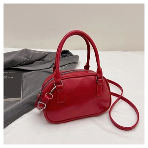 Détail d'un sac à main rouge en cuir PU brillant avec ferrures argentées sur tissu blanc