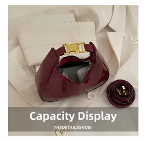 Detail of dark red patent leather crescent handbag with gold buckle and storage capacity