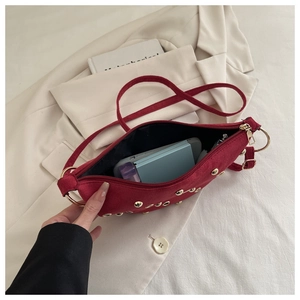 Vue de dessus d'un sac demi-lune rouge en daim avec clous dorés sur un blazer blanc