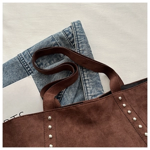 Detail of dark brown suede tote bag with decorative silver rivets and wide strap